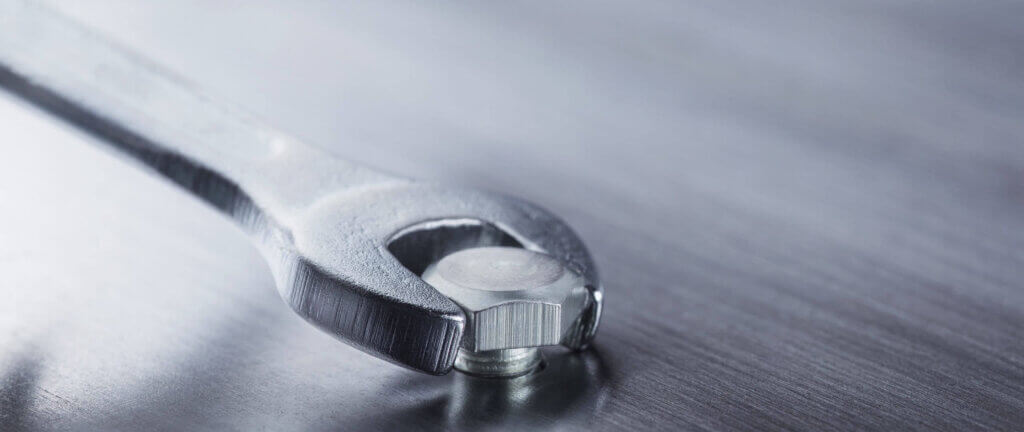 Schraubenschlüssel fixiert eine Schraube auf einer metallischen Oberfläche. Detailaufnahme von Werkzeugbenutzung.