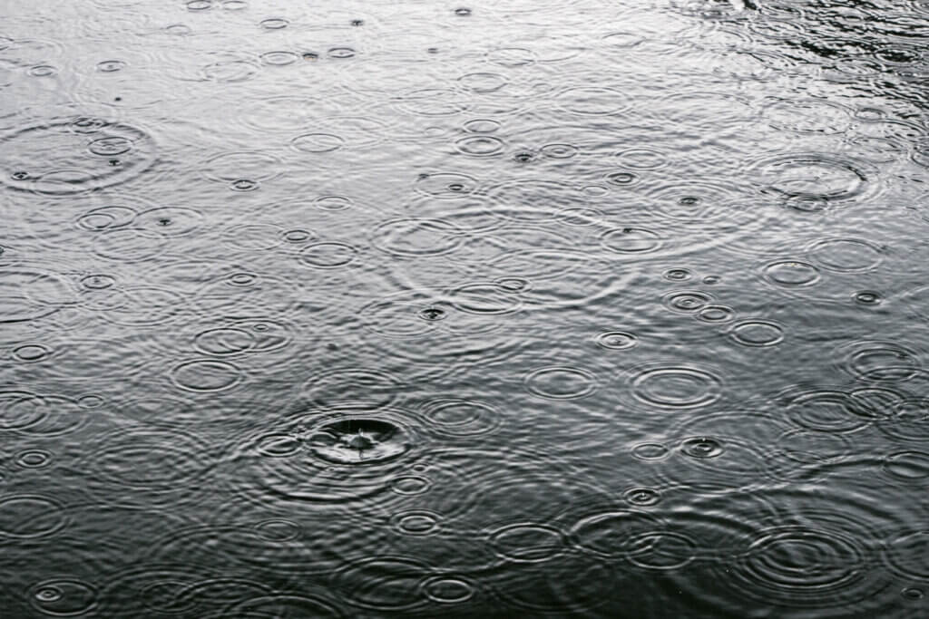 Regentropfen fallen auf die Wasseroberfläche und erzeugen kreisförmige Wellenmuster.