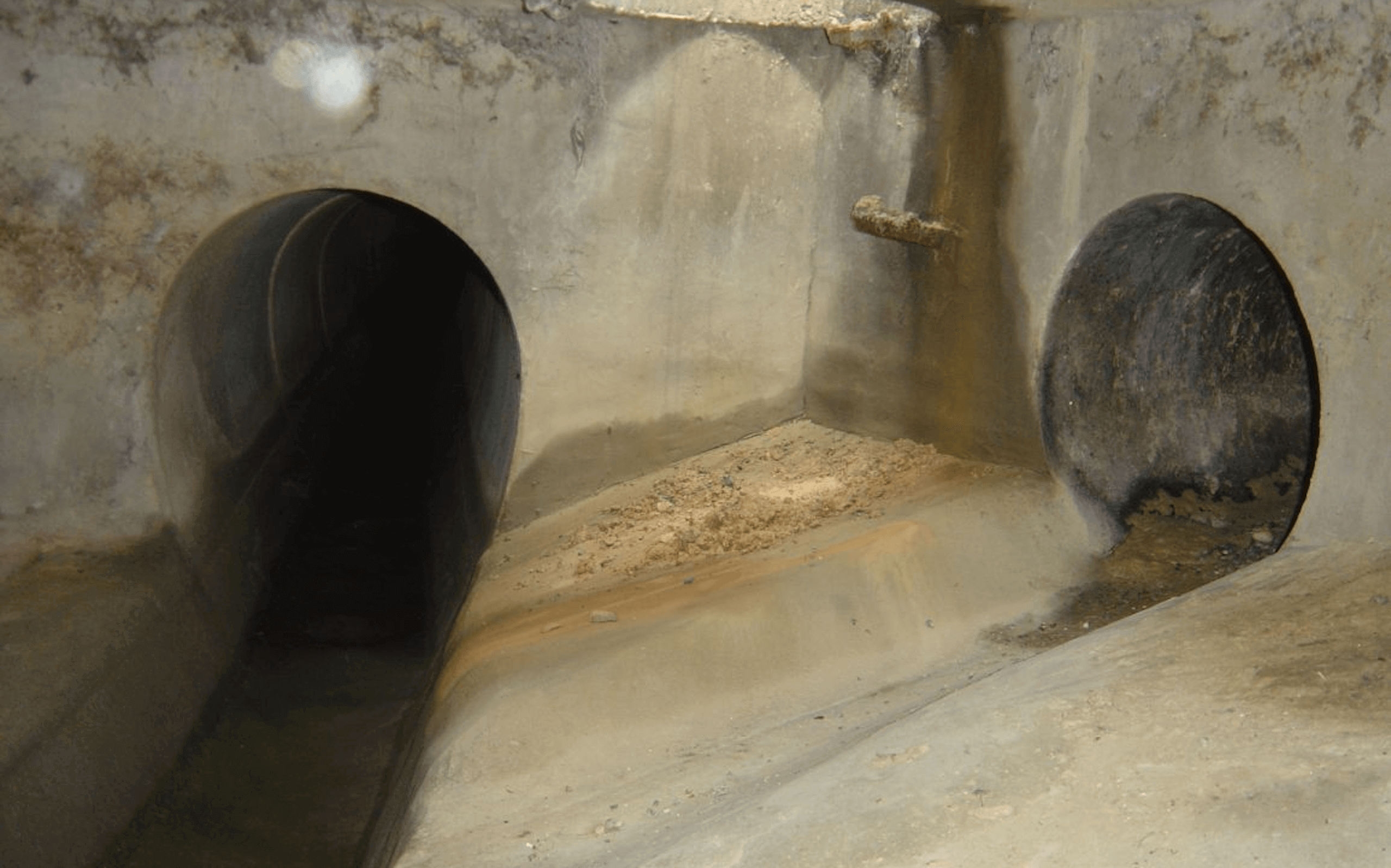Abwasserkanal mit zwei Tunnelöffnungen, Betonwände, feuchte Umgebung. Perfekt für urbane Erkundungen.