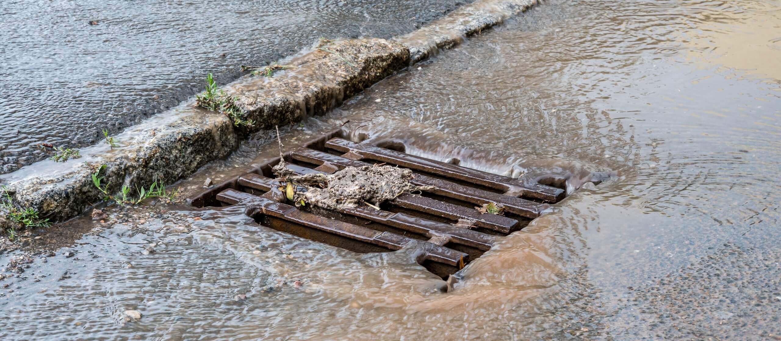 Straßenabfluss blockiert von Schmutz und Regenwasser, Risiko von Überschwemmung und schlechter Entwässerung.