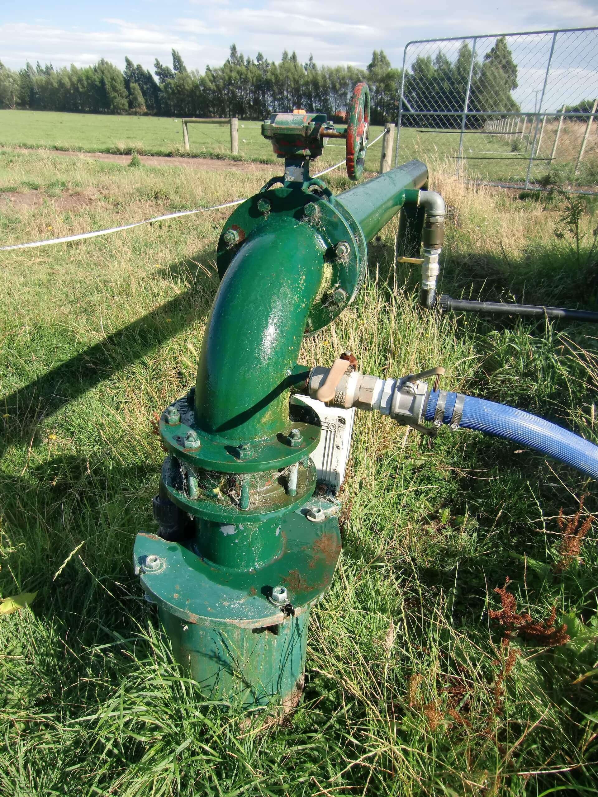 Grünes landwirtschaftliches Wasserrohr auf einem Feld, mit Ventil und Schlauch, unter blauem Himmel.